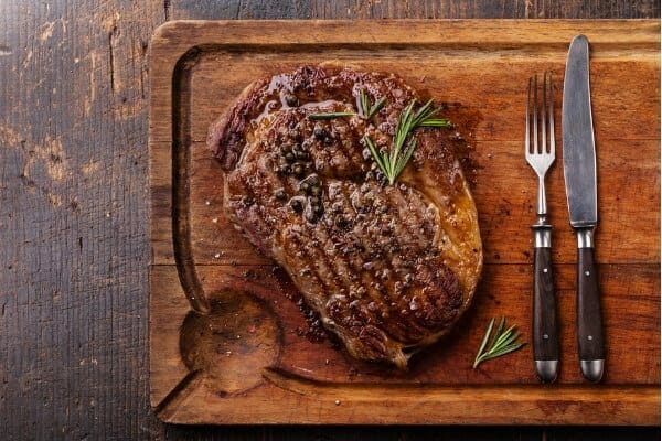 Grilled black angus steak ribeye on wooden board with knife and fork
