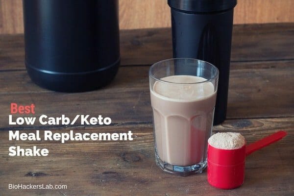 Glass of chocolate meal replacement powder shake on a wooden table next to a shaker and scoop