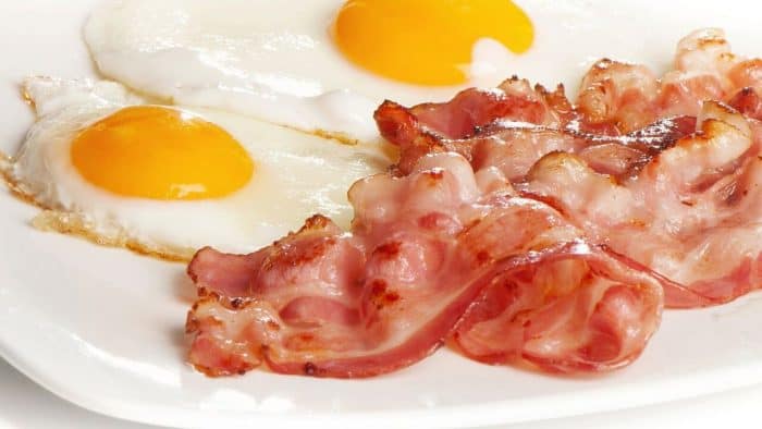 Two fried eggs and cooked bacon rashers on a plate