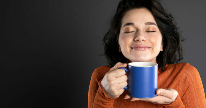 A smiling woman holding her coffee mug with her eyes closed