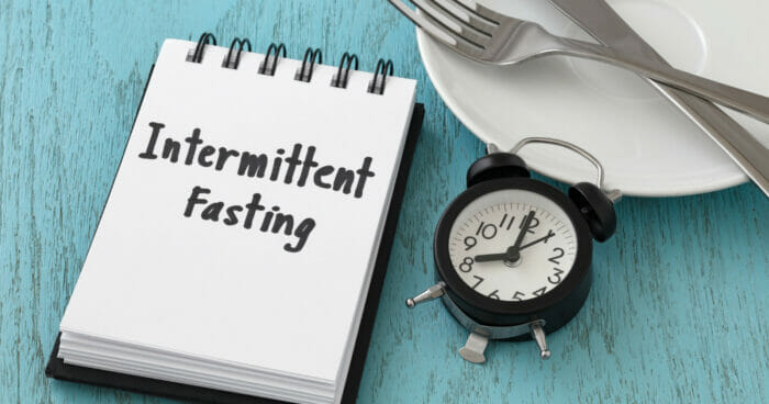 Notepad next to a clock and plate with the words intermittent fasting on it 